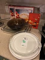 Stacked colored Pyrex bowls, various clear glass baking dishes, boxed fluted baking dish, boxed food net cover