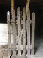 Full view of weathered barn gate showing wood slats, horizontal and diagonal braces, and iron hinges.