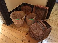 Overview of five wicker baskets on wooden floor, including picnic basket with closed hinges.