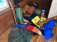 Various rolled sleeping bags, green rolled tent, blue rain poncho, colorful umbrella or poncho segments, and other camping gear.