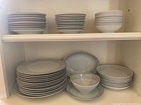 Stack of dinner plates, salad plates, and soup bowls arranged on a shelf showing silver scroll pattern and silver trim on white porcelain.