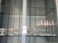 Display showing multiple liqueur glasses and tall wine glasses arranged on glass shelves.