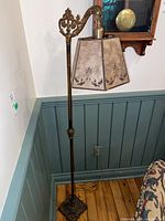 Full view of the metal floor lamp showing ornate base, vertical pole, articulated arm, and hanging shade.