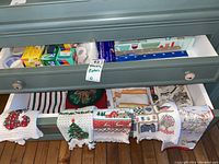 Drawer containing boxes of Ziploc bags, parchment paper, plastic wrap and other kitchen paper goods. Also several assorted festive tea towels, many with Christmas-themed designs.