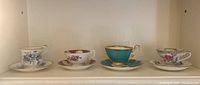 Four teacups and saucers in a row showing various floral and gold accent designs