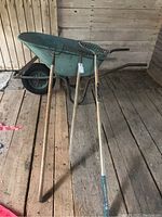 Full view of the garden tools lined up with the wheelbarrow behind them on wooden barn floor.