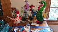View of seven blown glass animal figures including birds and a dog, displayed on a wooden surface near window light.