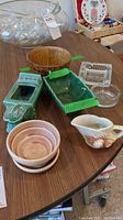 Overview of the collection showing pottery pieces including brown planter, green ashtrays, pink bowls, small pitcher with seashell design, and three glass ashtrays arranged on table.
