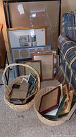 Photo showing assortment of picture frames stacked upright and lying down, with three wicker baskets holding many smaller frames.