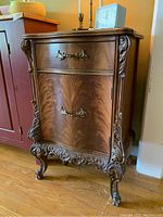Front angled view of ornate side cabinet showing detailed carvings and drawer/door handles.
