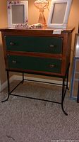 Full front and partial top view of the wooden chest showing two green drawers with wooden knobs and wrought iron legs.