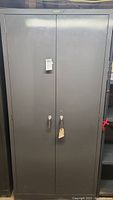 Front view of gray metal 2-door storage cabinet with locking handles and seller tag attached