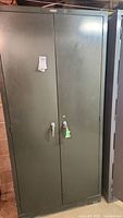 Front view of large green metal cabinet with two doors and handles, locked with key attached.