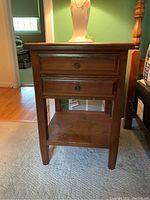 Front view of wooden nightstand with two drawers and lower shelf, place on carpet.