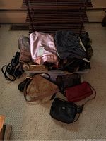 Various evening bags, clutches, and handbags piled in a plastic bin and some on the floor showcasing assorted bags in different colors and fabrics.