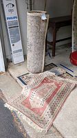 Rolled large area rug and one rectangular rug with red and beige design on garage floor