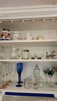 Shelf of assorted glassware and ceramics including stemware, pitchers, and canisters.