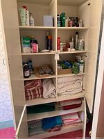 Tall white shelving unit with multiple shelves showing first aid and cosmetics items on the top shelves and folded bath towels on the lower shelves.