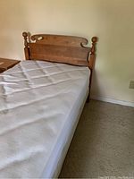 Twin bed with white mattress, wooden headboard with carved top and finial posts, metal frame visible on side.
