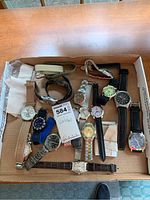 Wide view of all wristwatches in a cardboard box on a wooden surface, showing variety of straps and dial colors.