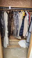 Closet rack with several fur coats, men's suits and dress coats hanging, some covered in plastic garment bags.