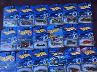 Full view of 18 carded Hot Wheels cars arranged for display on dark surface with visible blue packaging cards and plastic bubbles around the cars.