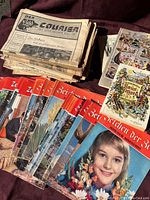 Photo of a stack of mid-20th century Bild Zeitung newspapers, several color magazines titled Beziehen der Zeit, and other publications spread on a purple fabric surface.
