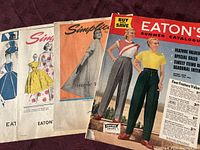 Four vintage paper catalogs and patterns laid out, showing front covers with colorful mid-century illustrations and photographs.