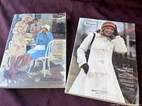 Two complete vintage Sears catalogs shown side by side on purple fabric background, covers visible with models dressed 1970s fashion styles