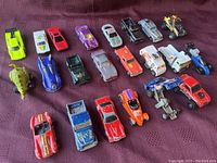 Photo showing all 22 die-cast vehicles arranged in rows on fabric surface, highlighting variety of colors, models, and worn condition.