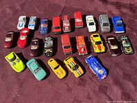 Photo showing all 23 die-cast toy vehicles arranged in rows on a fabric surface with various colors and designs visible.