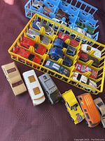 Photo showing multiple vintage Hot Wheels and die-cast vehicles arranged in blue and yellow plastic trays with some vehicles placed in front of the trays for detail view.