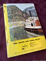 Front cover of 1958 Central Vancouver Island telephone book depicting a steamship and waterfront town. Yellow bottom border with directory title, locations and company name.