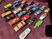 Photo showing the full lot of twenty vintage die-cast toy cars on a red textured fabric background with various models including muscle cars and race cars