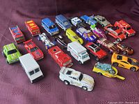 Photo of 22 assorted vintage die-cast vehicles arranged on a fabric surface.
