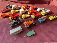 Overview of multiple vintage die-cast trucks and trailers in different colors and types arranged on a textured red surface.