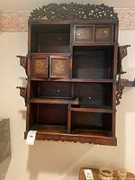 Front view of wall cabinet showing multiple cubbies, inlaid doors, carved top and scalloped apron