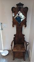 Full front view of antique oak hall tree showing carved crest, diamond mirror, seat and hooks