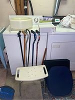 Overview of walking canes, shower chair, voice amplifier box, cushions placed on and around washing machine and dryer in garage.