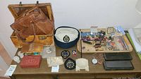 View showing assortment of vintage brown leather bags, navy cap, and table with pins, multi-tools, and other small items.