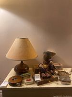 Full lot overview showing copper lamp with fabric shade, vintage dolls, assorted tins and cigar boxes arranged on a table.