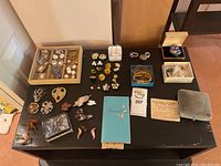 Full overview of all costume jewelry items displayed on a black surface showing multiple boxes and loose pieces including earrings and pins.