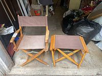 Two wooden directors chairs, one complete and one missing the back cloth, placed side by side. Located in garage setting with some clutter around.
