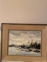 Framed painting showing snow-covered landscape with trees under cloudy sky