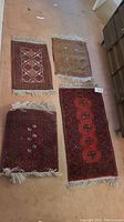 Four hand knotted rugs laid out on carpeted floor, varied colors and geometric patterns, show signs of wear and need cleaning.