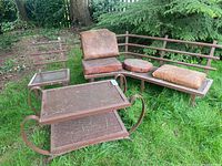 Curved metal patio bench with three cushions and metal outdoor table with two shelves; visible chipped paint and rust on metal surfaces, leather cushions worn