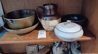 Display of stoneware bowls, jug, and lidded dish on shelf.