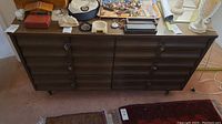Front view of vintage wooden dresser with six curved front drawers, dark finish, and metal handles. Various small items placed on top but not included.