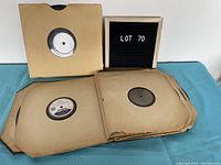 Assorted 78 RPM records in paper sleeves partially spread out on blue cloth surface with a small board reading 'LOT 70'