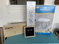 Lot with Dalmo bidet attachment box, bathtub and shower caddy box, and AquaSense shower chair box on a table with lot number board